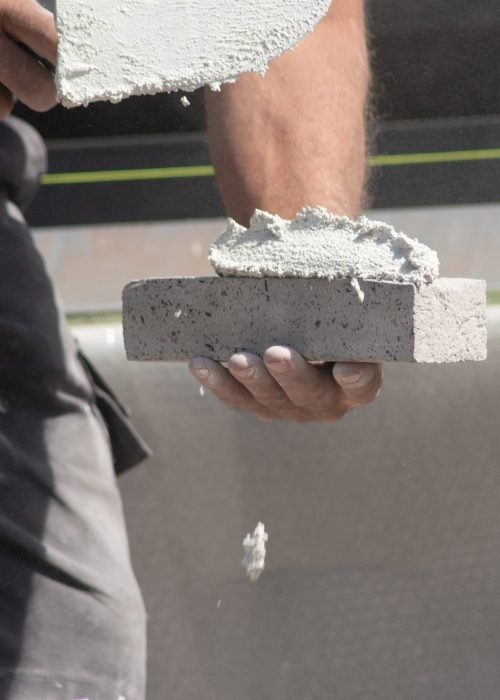 close up of the hands of a bricklayer applying cement mortar to a brick